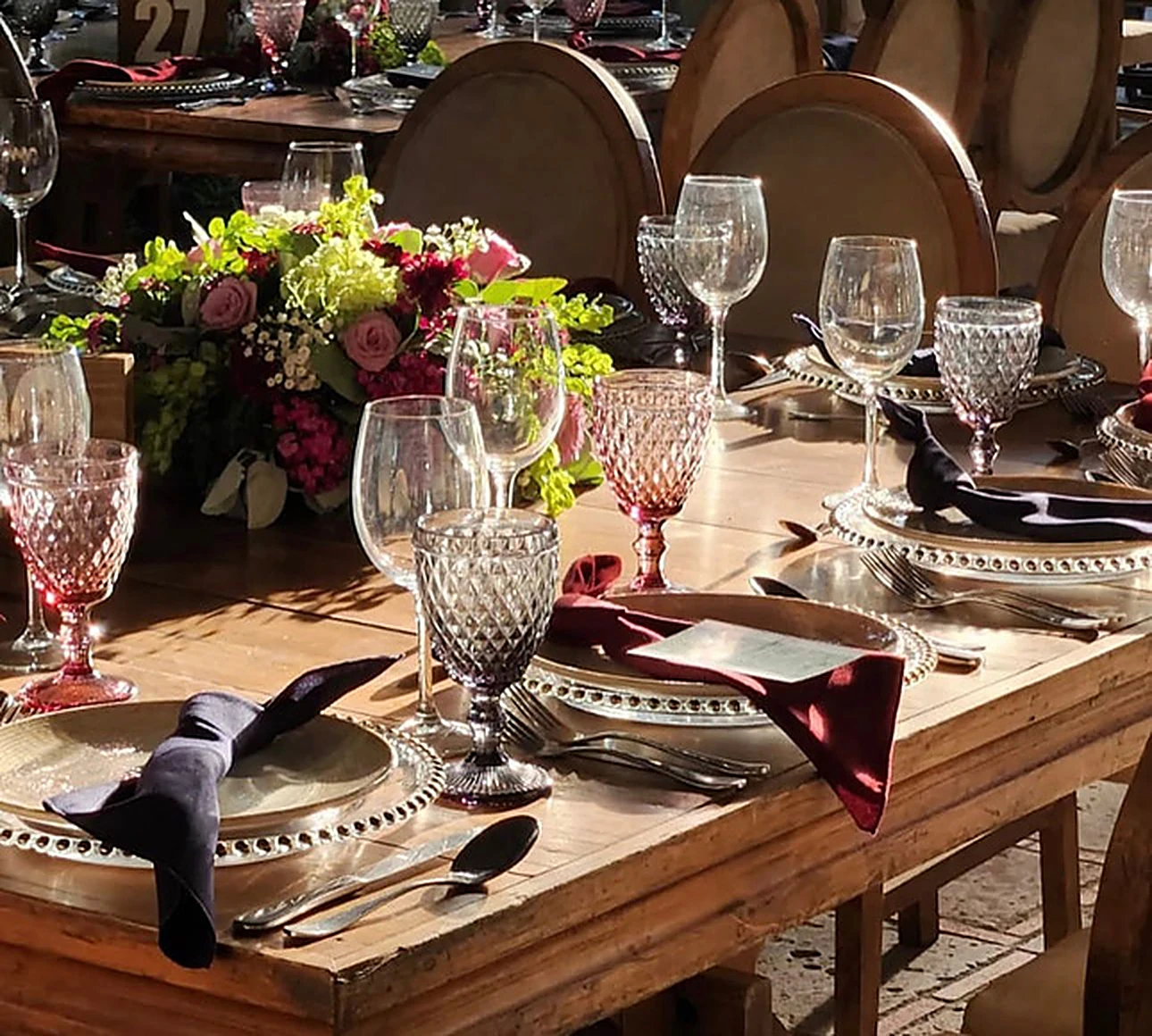 Mesa vestida con copas ámbar y centro floral en montaje al aire libre